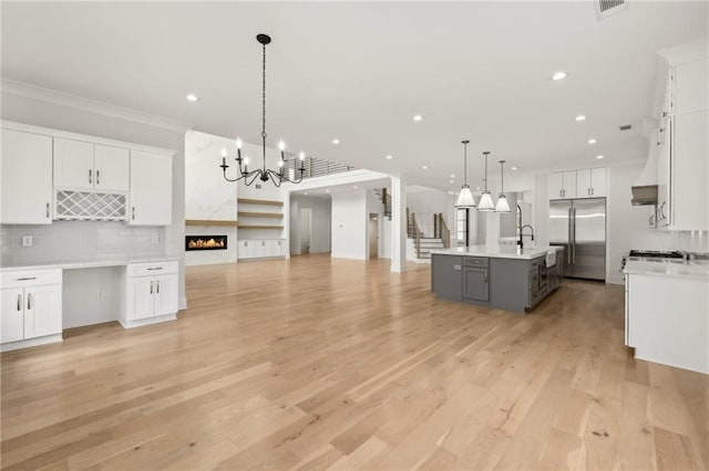 kitchen featuring light wood finished floors, stainless steel built in refrigerator, open floor plan, a center island with sink, and light countertops