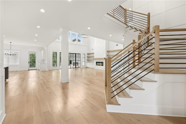 stairway with recessed lighting, decorative columns, a warm lit fireplace, and wood finished floors