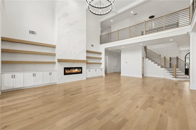 unfurnished living room featuring visible vents, stairway, a premium fireplace, light wood-style flooring, and a high ceiling