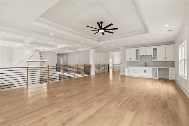 unfurnished living room with ornate columns, a tray ceiling, a sink, light wood-style floors, and crown molding