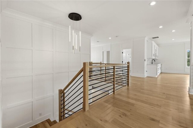 hallway featuring light wood finished floors, recessed lighting, crown molding, a decorative wall, and an upstairs landing