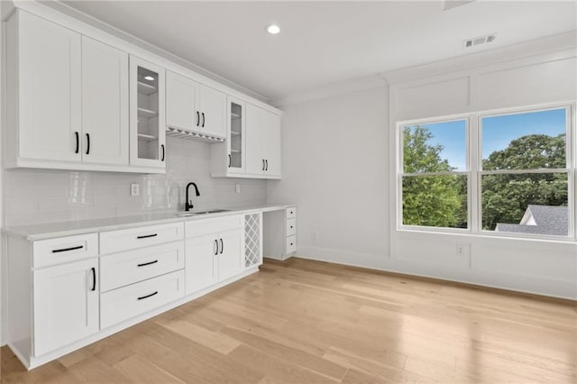 kitchen with glass insert cabinets, light countertops, decorative backsplash, light wood-style floors, and a sink