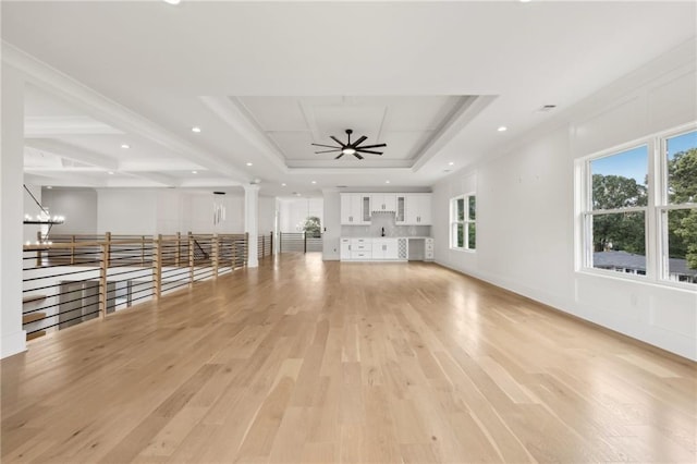 unfurnished living room with ornate columns, recessed lighting, light wood-style floors, a raised ceiling, and ceiling fan with notable chandelier