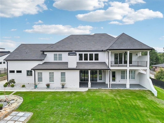 rear view of house featuring fence, a yard, a shingled roof, a balcony, and a patio area
