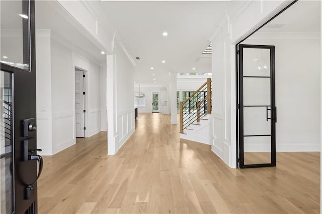 foyer entrance featuring stairway, light wood-style flooring, crown molding, and a decorative wall