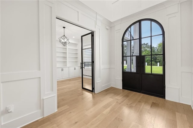 foyer entrance with a chandelier, light wood-style flooring, and a decorative wall