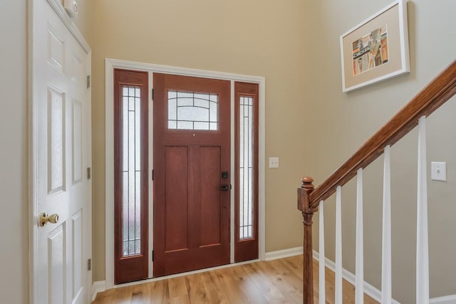 foyer entrance featuring light wood-style floors, stairway, and baseboards