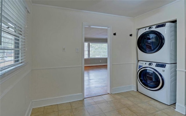 clothes washing area featuring stacked washer and clothes dryer, light tile patterned floors, laundry area, and crown molding