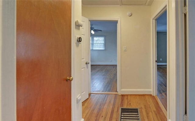 hallway featuring crown molding, baseboards, light wood finished floors, and visible vents
