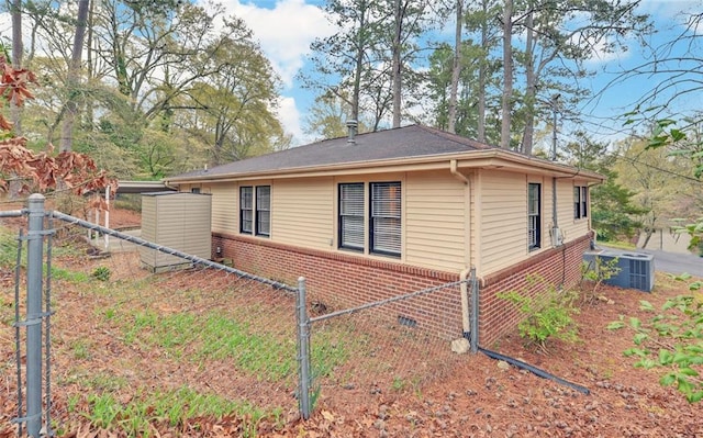 view of property exterior featuring brick siding, central air condition unit, and fence