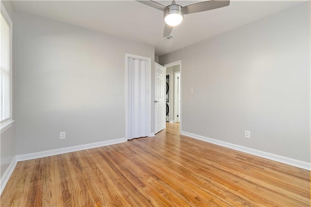 empty room with stacked washer / dryer, baseboards, and light wood-style flooring