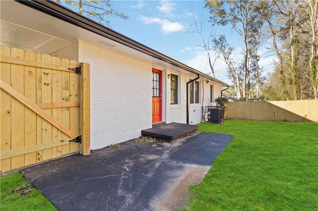 view of home's exterior featuring a yard, brick siding, central AC unit, and fence