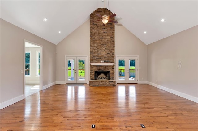 unfurnished living room with ceiling fan, a stone fireplace, light hardwood / wood-style floors, and high vaulted ceiling