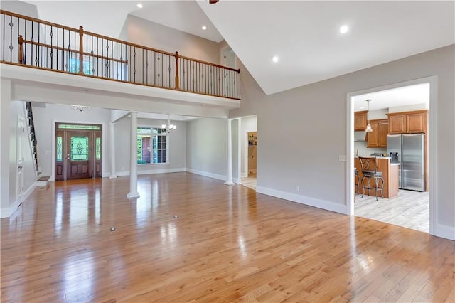 unfurnished living room featuring light hardwood / wood-style floors, ornate columns, high vaulted ceiling, and an inviting chandelier