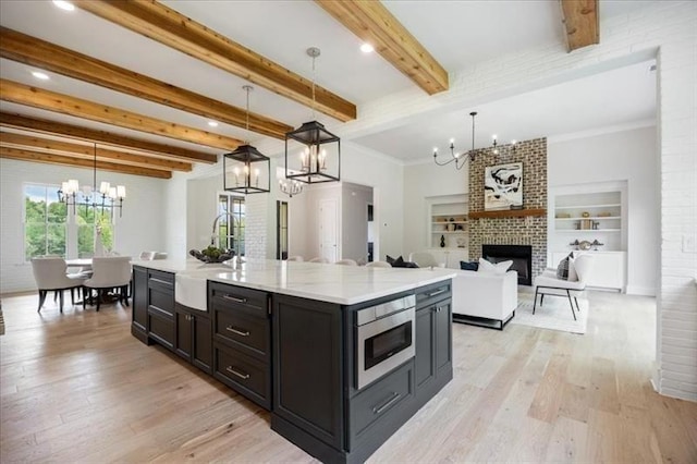 kitchen with a chandelier, a sink, stainless steel microwave, light wood-style floors, and hanging light fixtures