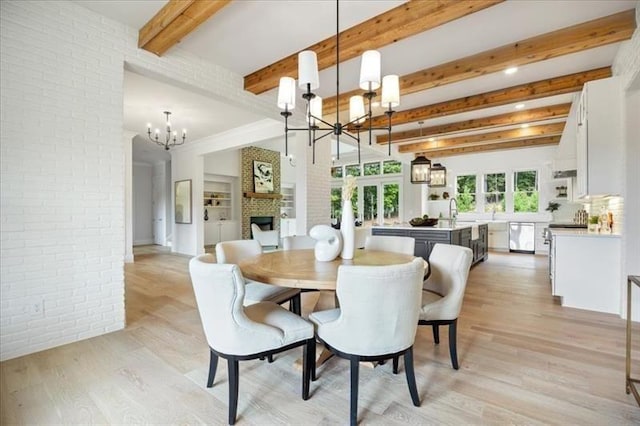 dining area featuring a chandelier, light wood-type flooring, brick wall, a large fireplace, and beamed ceiling
