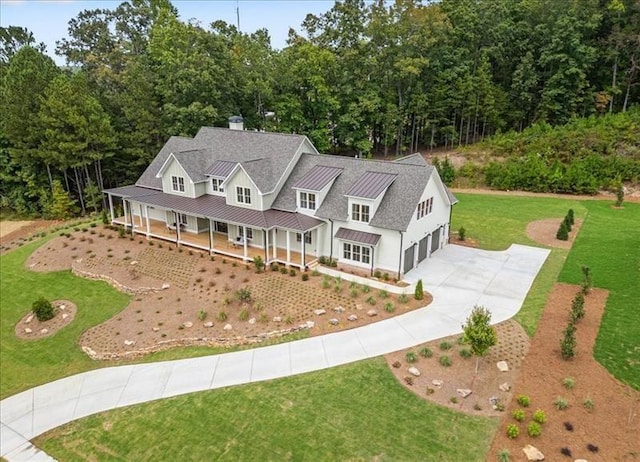 view of front of home featuring a porch, concrete driveway, a front lawn, a standing seam roof, and metal roof