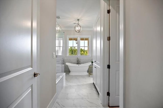 bathroom featuring marble finish flooring, a soaking tub, a chandelier, and crown molding