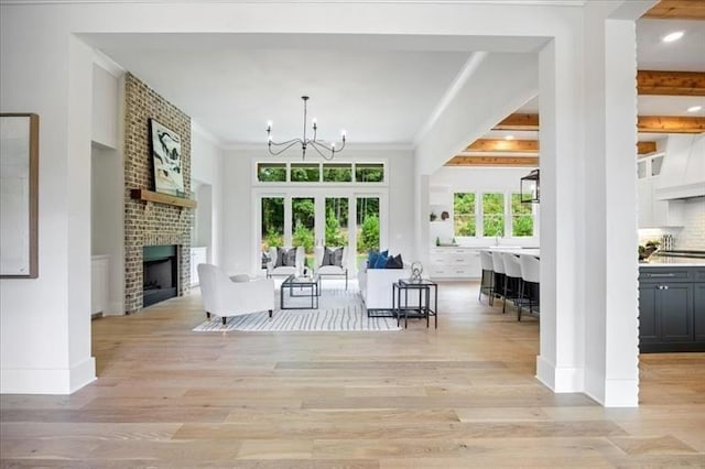 living area featuring a chandelier, light wood-style flooring, a brick fireplace, baseboards, and ornamental molding