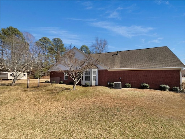 rear view of house featuring roof with shingles, brick siding, a lawn, and fence