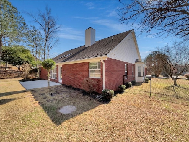 view of side of property featuring brick siding, a yard, a patio, a chimney, and fence