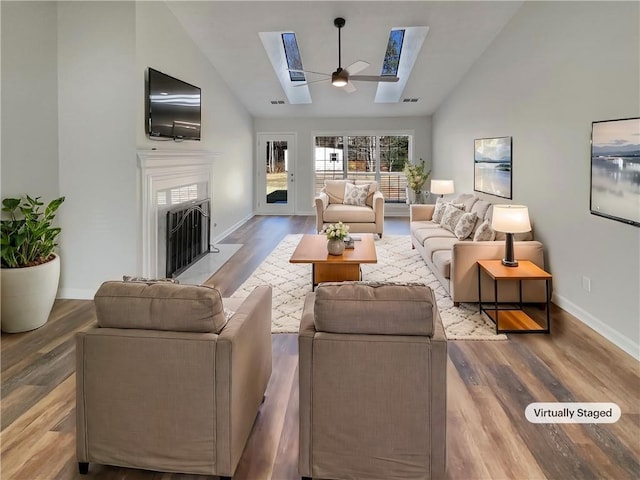 living area with a skylight, a fireplace with flush hearth, wood finished floors, high vaulted ceiling, and baseboards