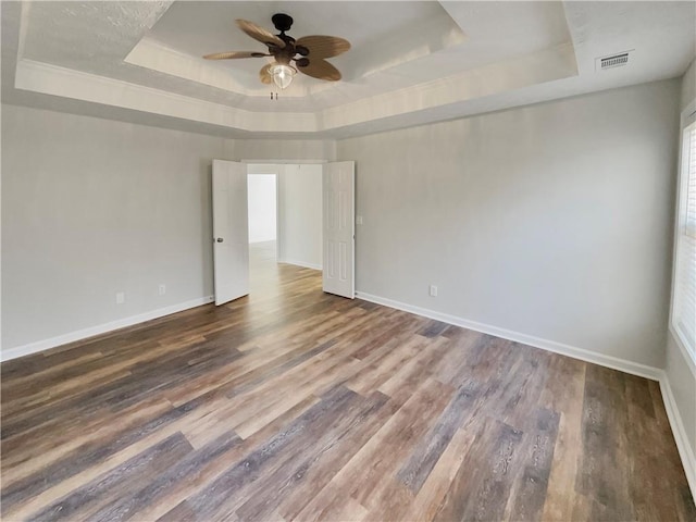 empty room with baseboards, visible vents, a raised ceiling, and wood finished floors