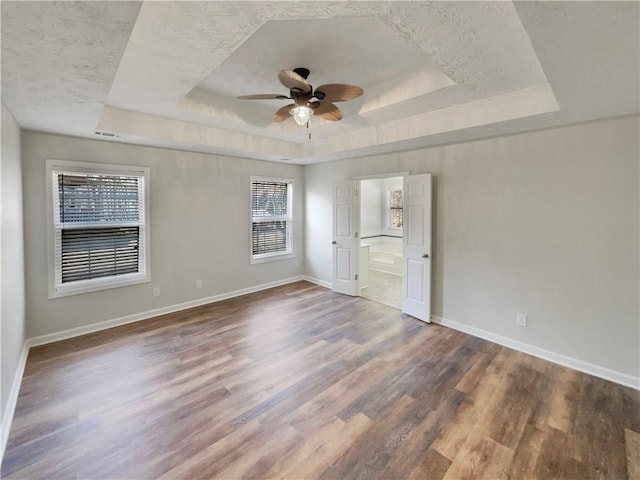 unfurnished bedroom featuring baseboards, a tray ceiling, and wood finished floors