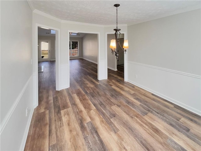 unfurnished dining area featuring a textured ceiling, ornamental molding, wood finished floors, and baseboards