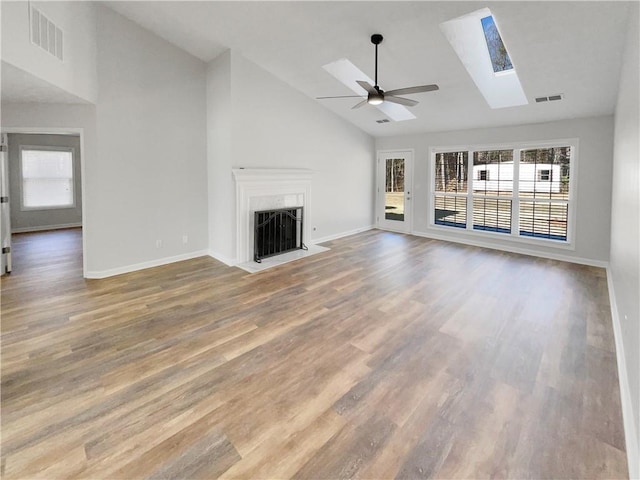 unfurnished living room featuring a skylight, a fireplace with flush hearth, visible vents, and wood finished floors