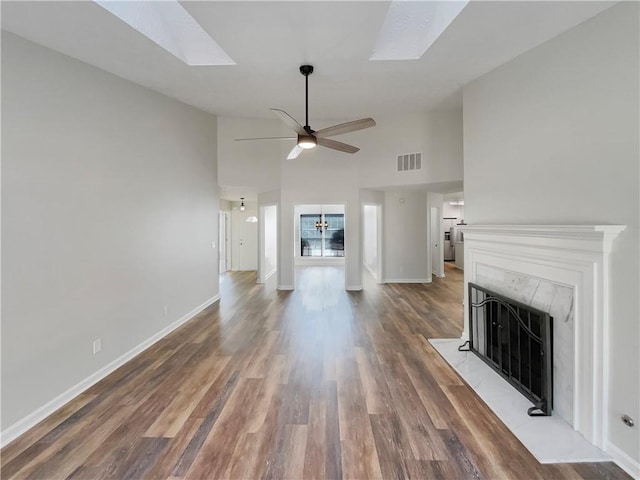 unfurnished living room featuring a skylight, visible vents, a fireplace with raised hearth, a ceiling fan, and wood finished floors