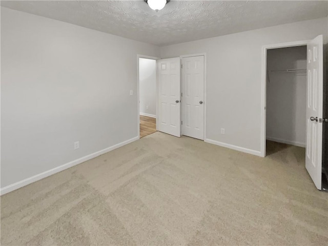 unfurnished bedroom featuring carpet floors, a textured ceiling, baseboards, and a spacious closet