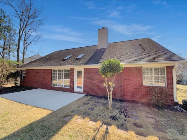 rear view of property with a patio area, roof with shingles, a chimney, and brick siding