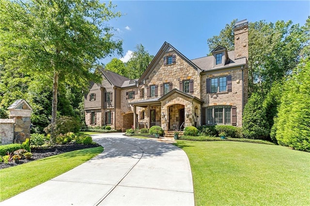 view of front of property with concrete driveway, stone siding, a chimney, a front lawn, and brick siding