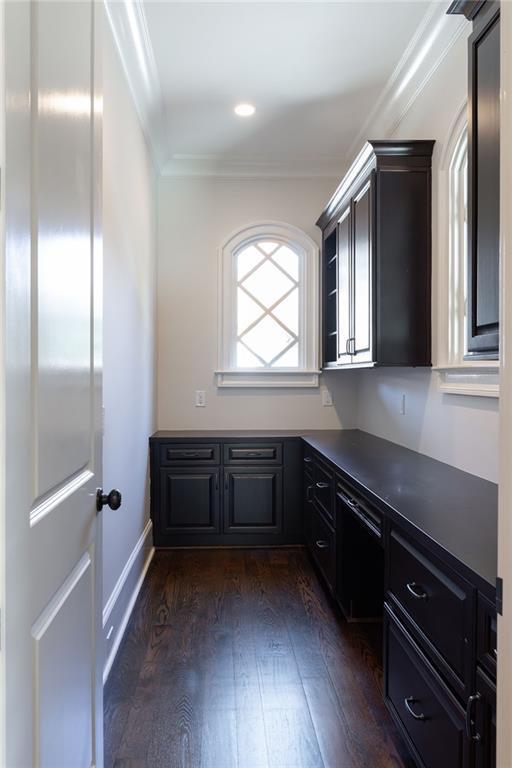 unfurnished office featuring dark wood-style floors, baseboards, ornamental molding, and built in desk