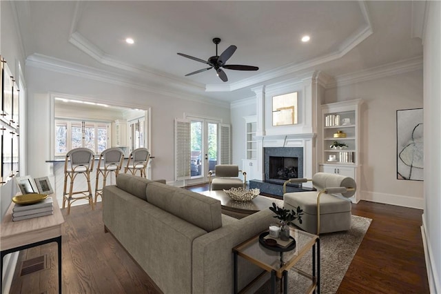 living room with dark wood-type flooring, a high end fireplace, baseboards, a tray ceiling, and crown molding