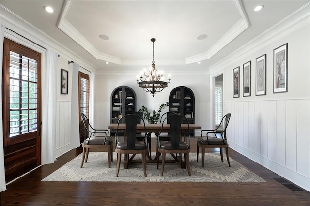 dining room with a wainscoted wall, crown molding, a raised ceiling, dark wood-type flooring, and a chandelier