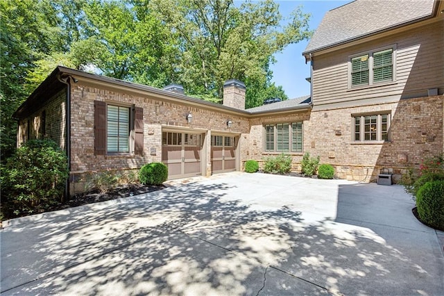 view of front of home with a garage, driveway, a chimney, and brick siding