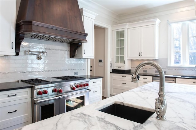 kitchen with dark stone countertops, double oven range, white cabinetry, and premium range hood