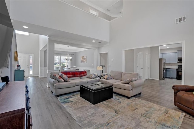 living room with ornamental molding, light hardwood / wood-style flooring, a chandelier, and a high ceiling