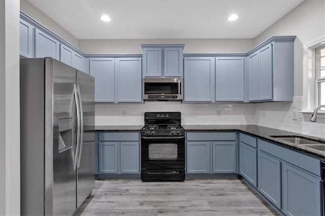 kitchen featuring appliances with stainless steel finishes, light wood-type flooring, decorative backsplash, sink, and dark stone countertops