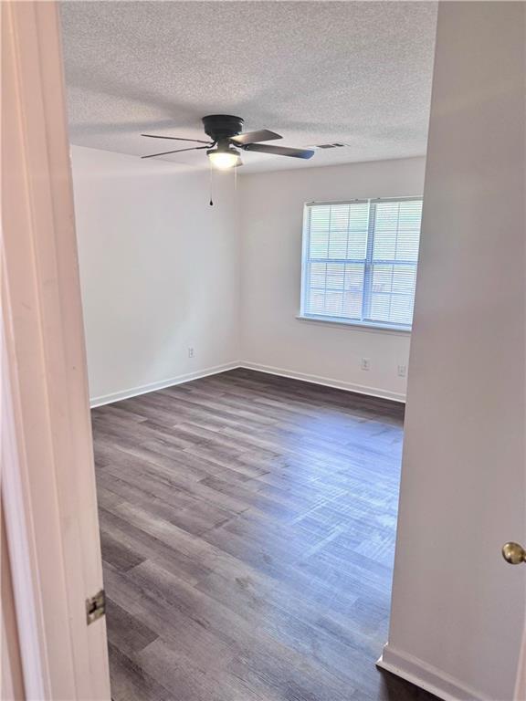 spare room featuring dark wood-style floors, a textured ceiling, baseboards, and a ceiling fan