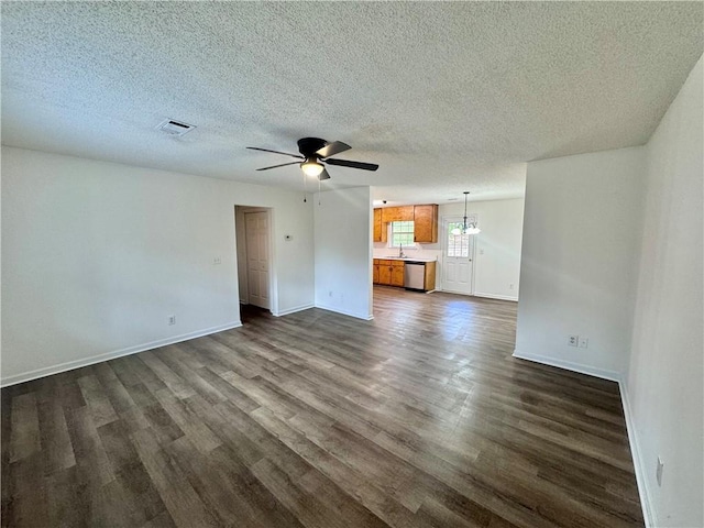 unfurnished living room featuring visible vents, dark wood-type flooring, ceiling fan with notable chandelier, a textured ceiling, and baseboards