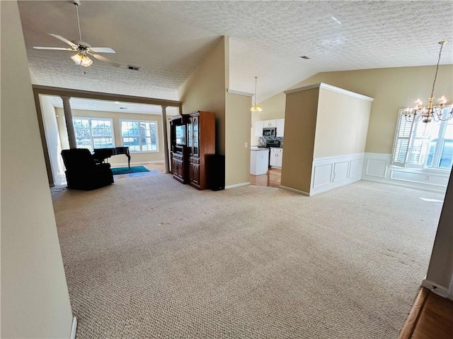 unfurnished living room with vaulted ceiling, ceiling fan with notable chandelier, and light colored carpet