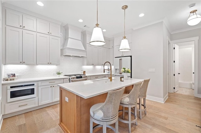 1010 Fendley St, Woodstock, GA 30188 - kitchen with stainless steel appliances, premium range hood, a sink, light wood-style flooring, and ornamental molding