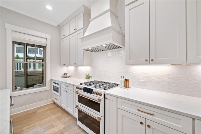 1010 Fendley St, Woodstock, GA 30188 - kitchen with premium range hood, double oven range, light wood-style flooring, baseboards, and white cabinets