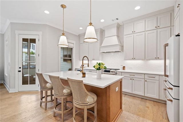 1010 Fendley St, Woodstock, GA 30188 - kitchen with freestanding refrigerator, premium range hood, light wood-style flooring, light countertops, and a center island with sink