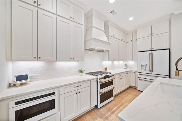 1010 Fendley St, Woodstock, GA 30188 - kitchen featuring high quality appliances, custom exhaust hood, white cabinetry, light wood-style flooring, and backsplash