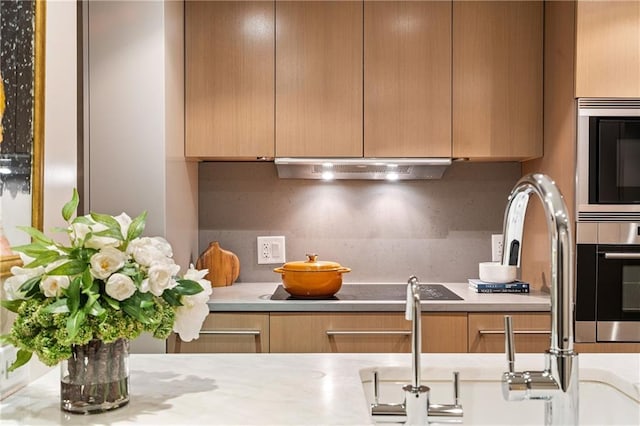 kitchen featuring built in microwave, backsplash, ventilation hood, and stainless steel oven