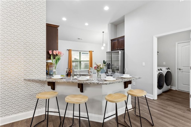 kitchen featuring separate washer and dryer, stainless steel fridge, a kitchen bar, dark wood-type flooring, and kitchen peninsula